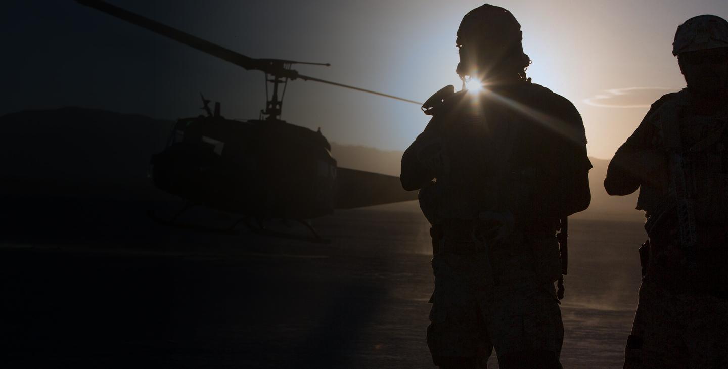 Two silhouettes of soldiers watching a helicopter take off